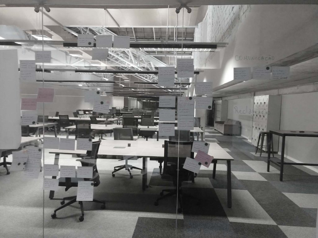 A wall of glass with some post-its. Some tables and chairs are shown on background through the glass.